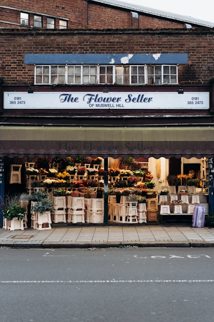 The storefront of The Flower Seller of Muswell Hill, featuring an array of fresh floral arrangements displayed on white wooden tables and shelves. The bouquets include a variety of flowers such as yel